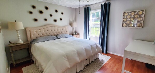 A bedroom with a tufted headboard bed, two bedside tables with lamps, a window with curtains, and a decorative wall piece. - New Listing! Perfect Lake Bowen Home With Lake Views, Decks, & Dock (Inman)