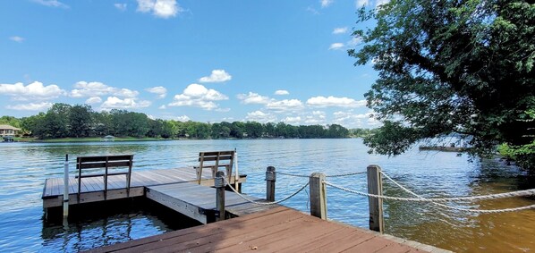 Un muelle de madera que se extiende hacia un lago tranquilo, con un banco y una barandilla de cuerda.