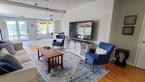 A spacious living room with a sofa set, a coffee table, and a TV mounted on the wall.