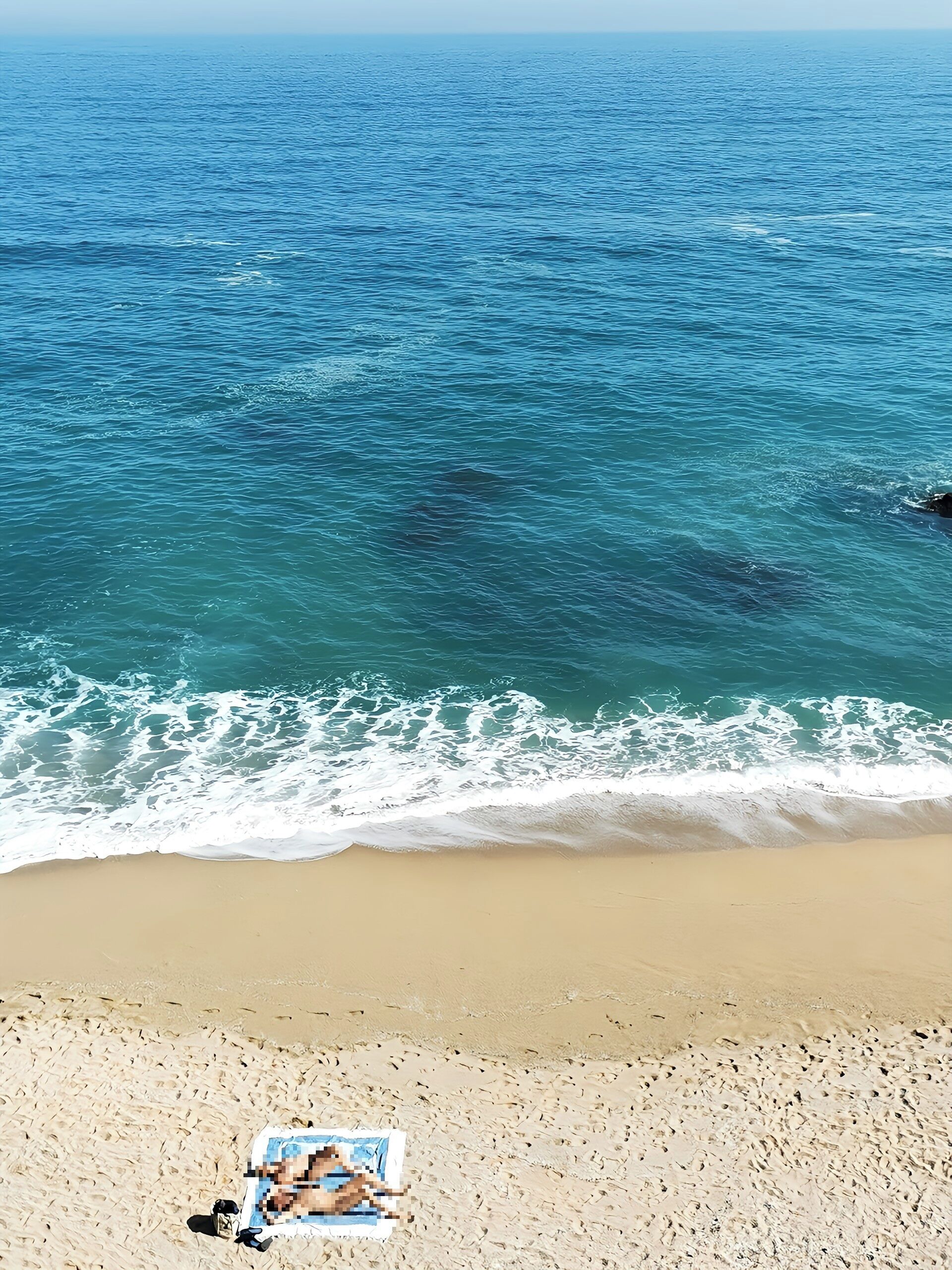 A beach with a clear view of the ocean and a towel on the sand.