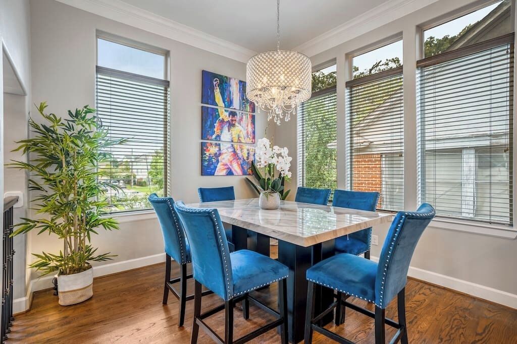 Un comedor con una mesa de mármol, sillas tapizadas en azul, una araña y obras de arte en la pared.
