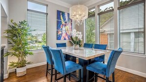 Un comedor con una mesa de mármol, sillas tapizadas en azul, una araña y obras de arte en la pared.