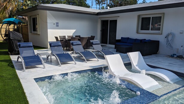 Une piscine avec des chaises longues et un espace patio aménagé avec du mobilier d’extérieur.