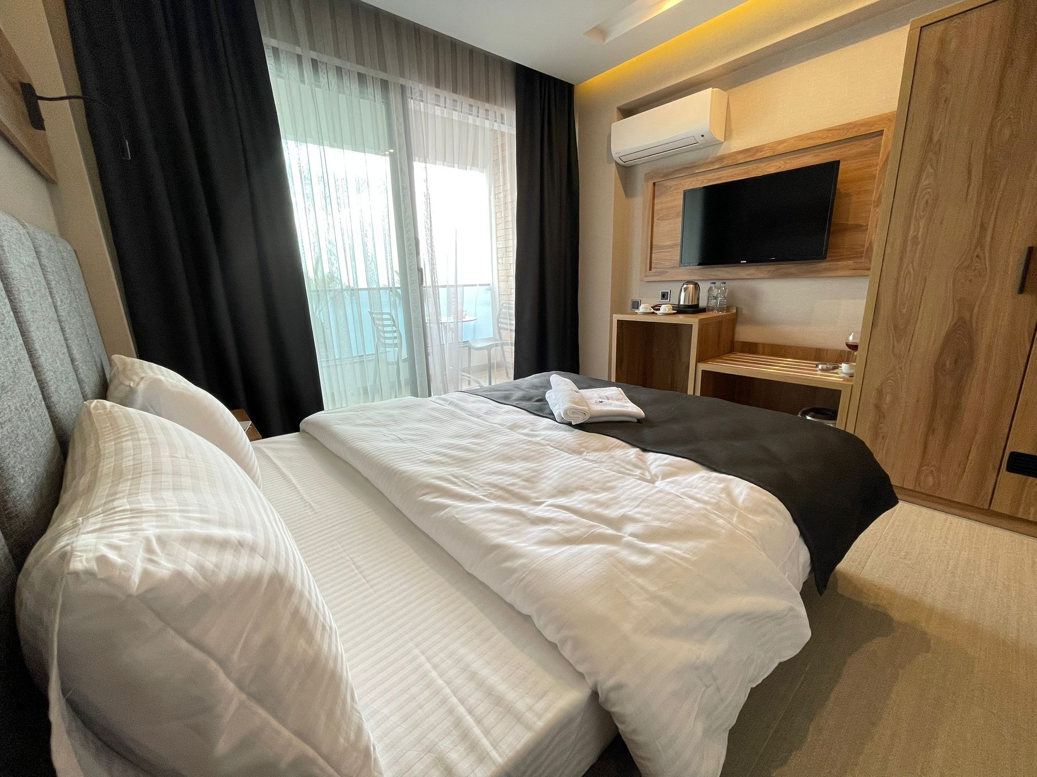 A hotel room with a large bed, a TV mounted on the wall, and a small table with a kettle and cups.