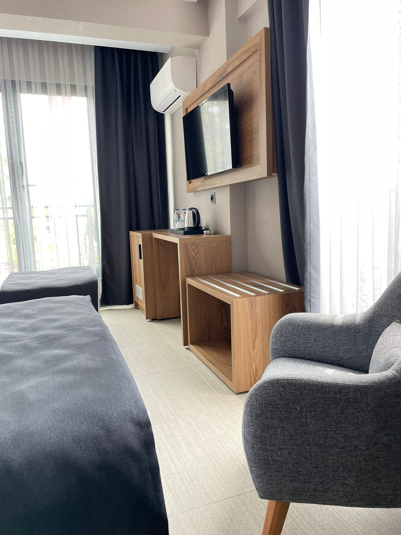 A hotel room with a bed, a TV, a wooden side table, and a chair.
