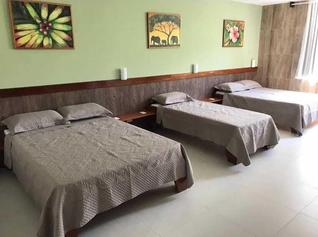 A hotel room with three single beds, a wooden headboard, and artwork on the walls.