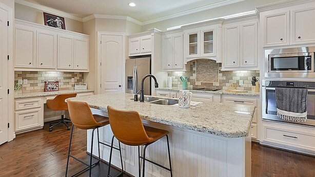Una cocina amplia con muebles blancos, encimera de granito y horno de acero inoxidable.