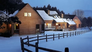 Een houten blokhut met een sneeuwbedekte dak, een houten hek en uitzicht op de omliggende bomen.