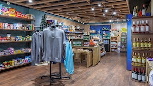 Een kledingwinkel met rekken vol kleding, een etalagepop en schappen met snacks en drankjes.