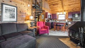 Een gezellig cabin interieur met houten details, een bank, een rode fauteuil, een eethoek en een keuken.