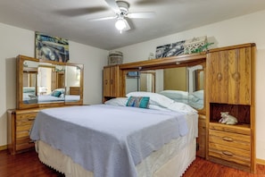Ein Schlafzimmer mit einem Bett, Holzmöbeln, einem Deckenventilator und Wandspiegeln.