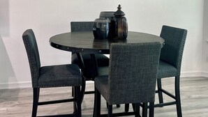 Een eetgedeelte met een ronde tafel, vier stoelen en een lijst met een schilderij erboven.