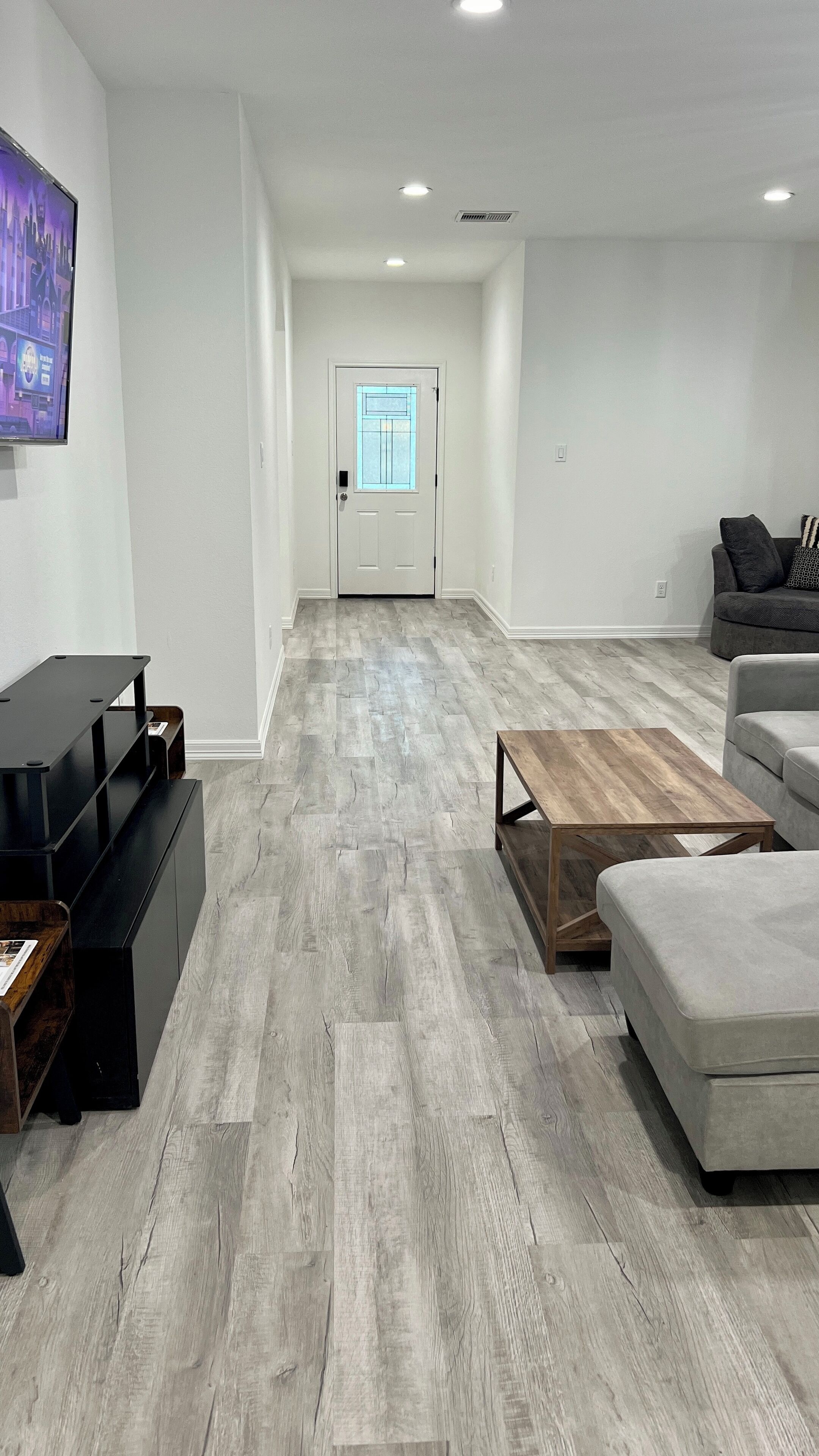 Een moderne woonkamer met een grijze houten vloer, een grijze bank, een houten salontafel en een aan de muur bevestigde televisie.