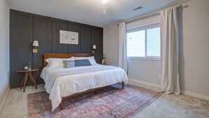 Een slaapkamer met een bed, een vloerkleed, twee nachtkastjes en een raam met gordijnen.
