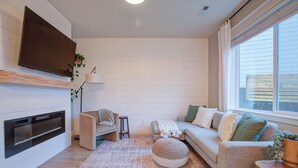 Een moderne woonkamer met een open haard, een bank, een salontafel en een televisie aan de muur.