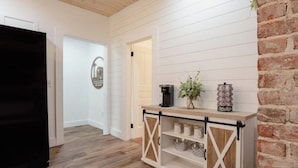 A hallway with a white wooden wall, a black refrigerator, a coffee machine, and a decorative item on a wooden shelf.