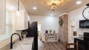 A kitchen with a wooden ceiling, a black refrigerator, a white cabinet, and a TV mounted on the wall.