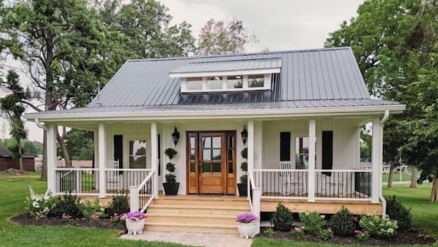 A single-story house with a porch, a front door, and a small garden area with potted plants.