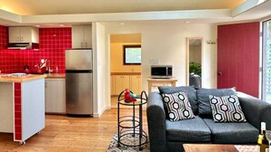 A modern kitchen with red tiles, a stainless steel refrigerator, and a dining area with a grey sofa and patterned cushions.