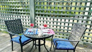 A round table with two chairs, a white pitcher, and two red glasses on a wooden deck.