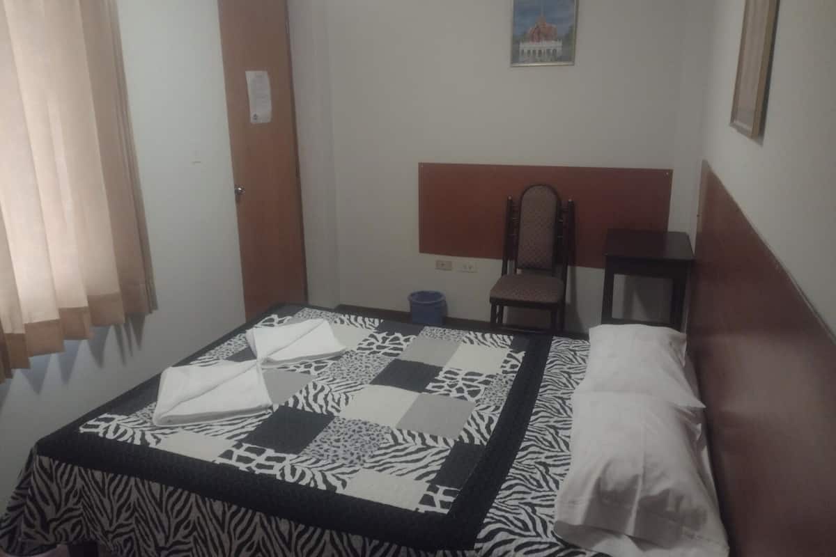 Ein Schlafzimmer mit einem bettenüberzug mit ZEBRA-MUSTER, einem hölzernen Kopfteil, einem Stuhl, einem kleinen Tisch und einem Bild an der Wand.