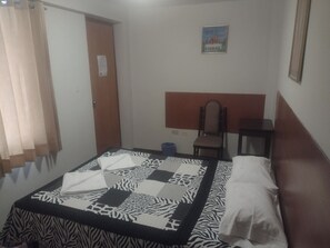 Quarto com colcha estampada de zebra, cabeceira de madeira, uma cadeira, uma mesinha e um quadro na parede.