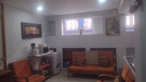 A living room with a sofa set, a coffee table, a microwave, and a small refrigerator. There are two windows with curtains, a painting on the wall, and a door on the left. - C. Deán Valdivia 120 (Arequipa)