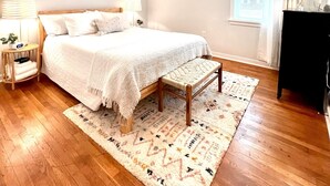 Une chambre à coucher comprenant un lit, un ventilateur de plafond, une table de chevet avec une lampe, un tapis et une fenêtre avec des rideaux.