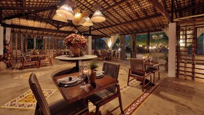 Un comedor interior con mesas y sillas de madera, una mesa redonda central con un jarrón de flores y lámparas colgantes.