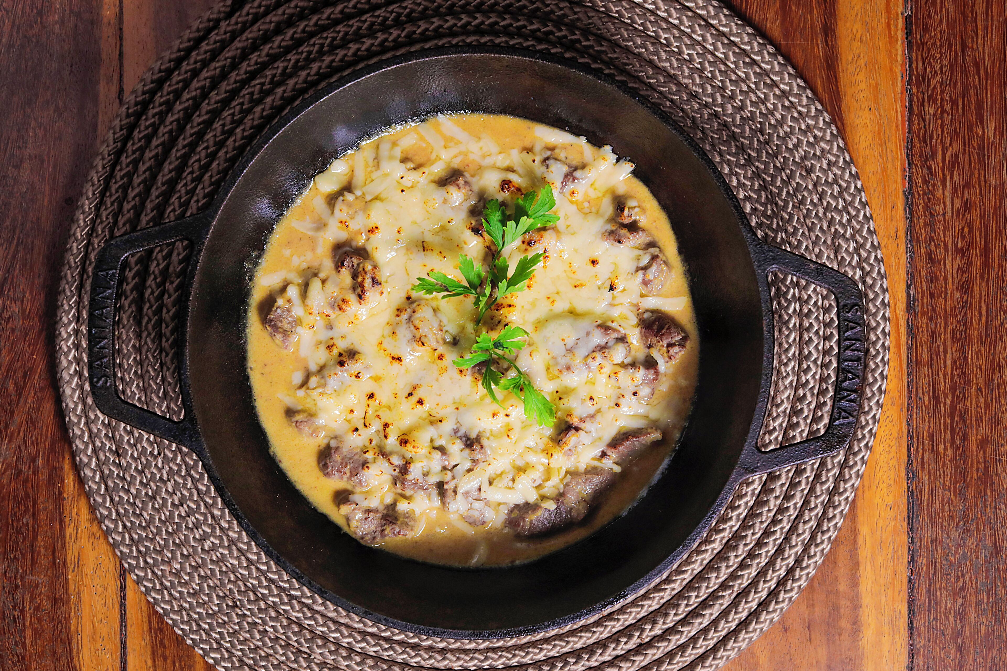 A bowl of soup with cheese and herbs on a woven mat.
