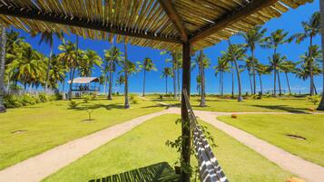 A tropical resort with a thatched-roof pavilion, palm trees, and a clear view of the ocean.