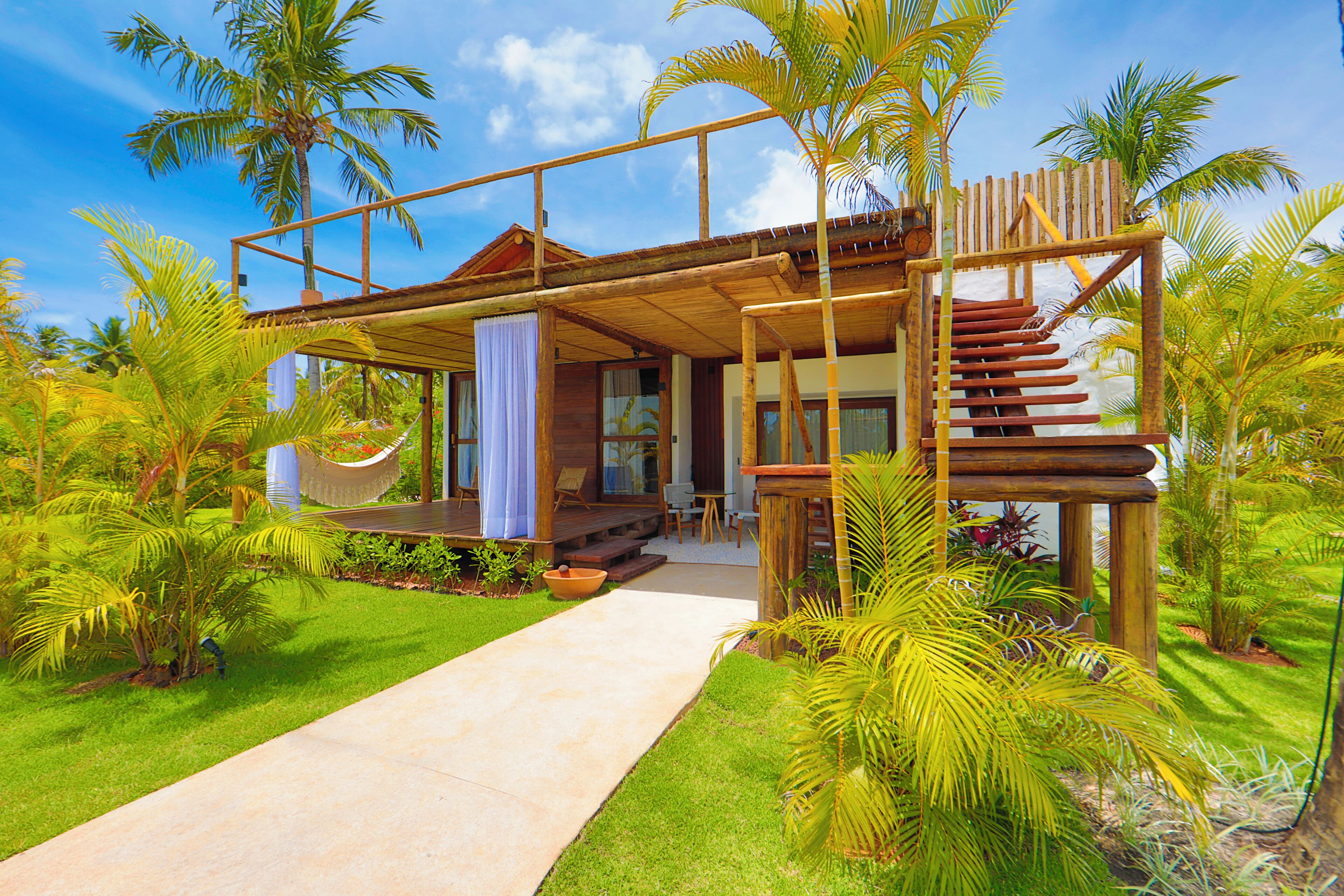 A modern house with a wooden deck, a hammock, and a staircase leading to a second level.