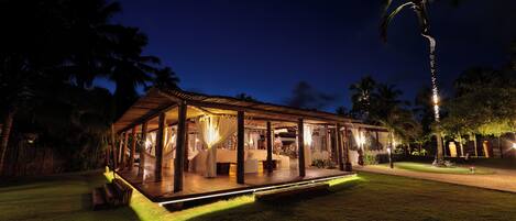 A covered outdoor area with a wooden deck, benches, and a well-lit pathway.