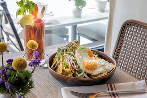 A dining table with a bowl of nachos, a glass of iced tea, and a small plant with yellow flowers. - The Benson Hotel and Faculty Club (Aurora)