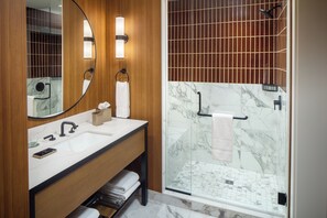 A modern bathroom with a wooden vanity, a glass shower enclosure, and marble tiles. - The Benson Hotel and Faculty Club (Aurora)