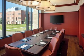 A conference room with a long table, leather chairs, and a TV on the wall. - The Benson Hotel and Faculty Club (Aurora)