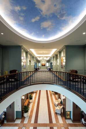 A hotel lobby with a central atrium, a curved balcony, and a ceiling mural. - The Benson Hotel and Faculty Club (Aurora)