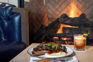 A dining table with a plate of food, a glass of drink, and a leather couch. - The Benson Hotel and Faculty Club (Aurora)