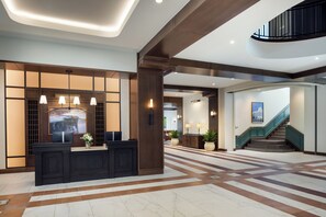 A spacious lobby with a reception desk, a staircase, and a large window with a cityscape view. - The Benson Hotel and Faculty Club (Aurora)