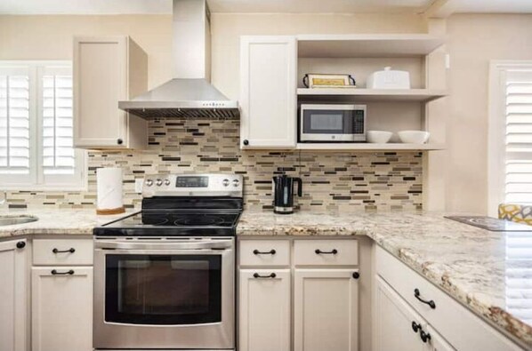 Modern kitchen with central island, stainless steel stove, and oven, featuring light-colored cabinetry and a mosaic backsplash.