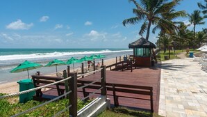 Terraza de madera con bancos y sombrillas verdes con vista a la playa.