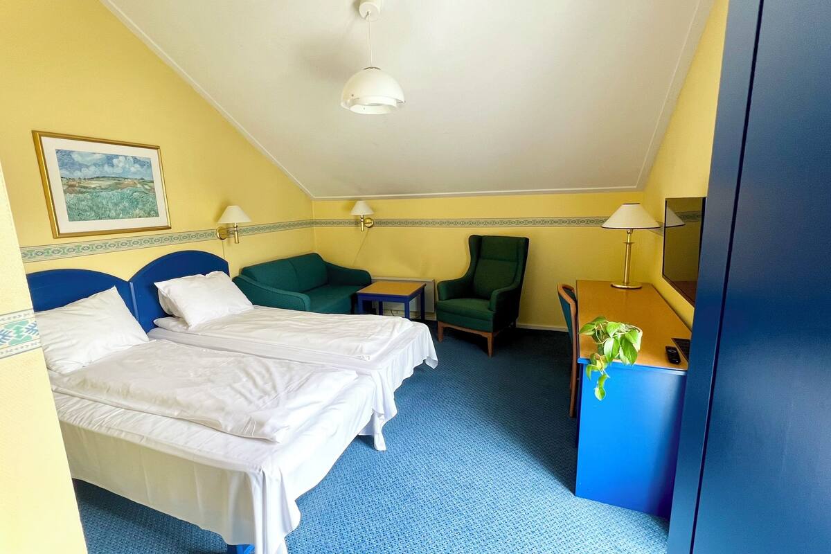 Une chambre d’hôtel avec deux lits, un bureau, une chaise, une lampe et un tableau au mur.