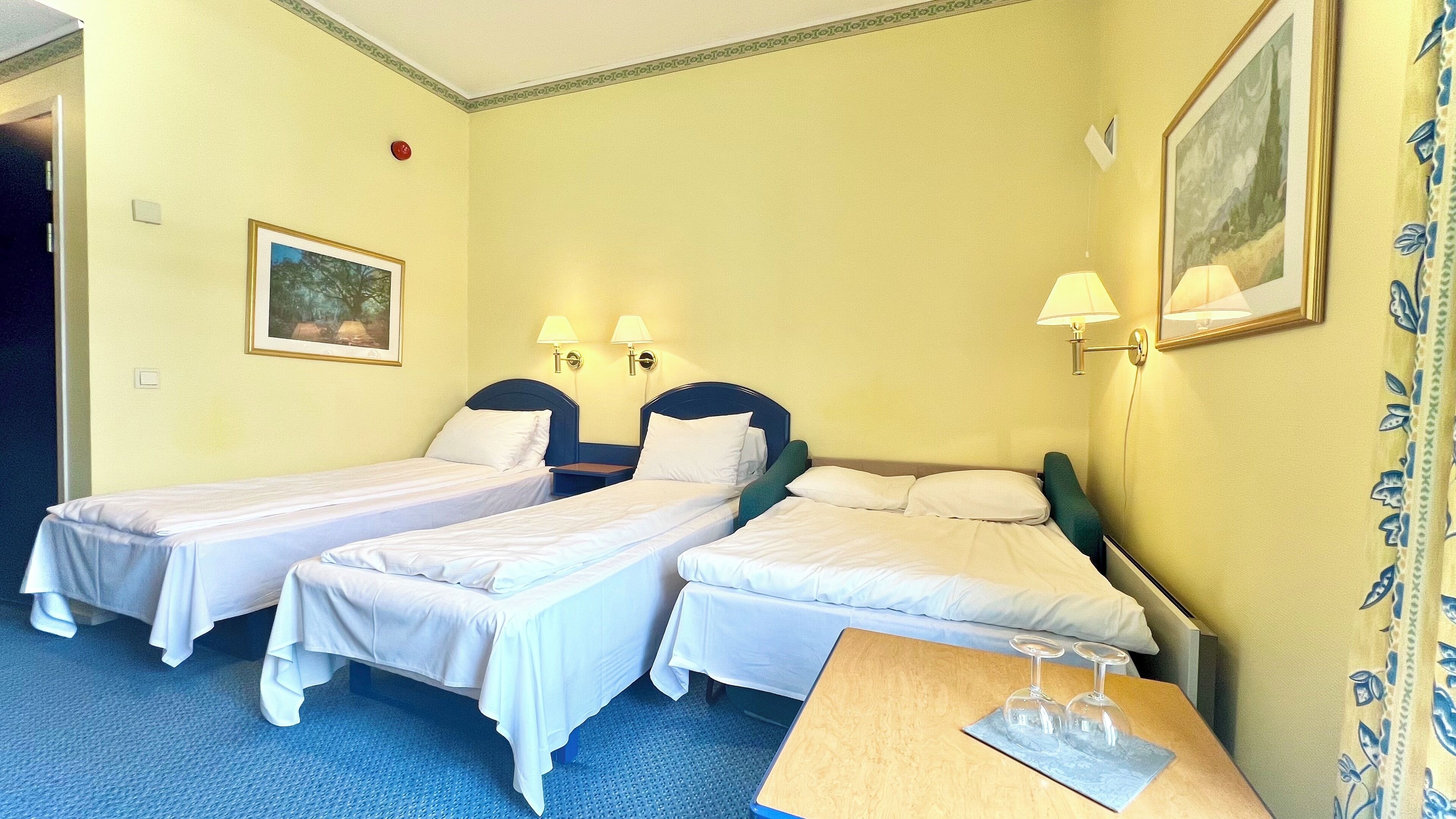 A hotel room with two single beds, a wooden side table with a wine glass, and a painting on the wall.