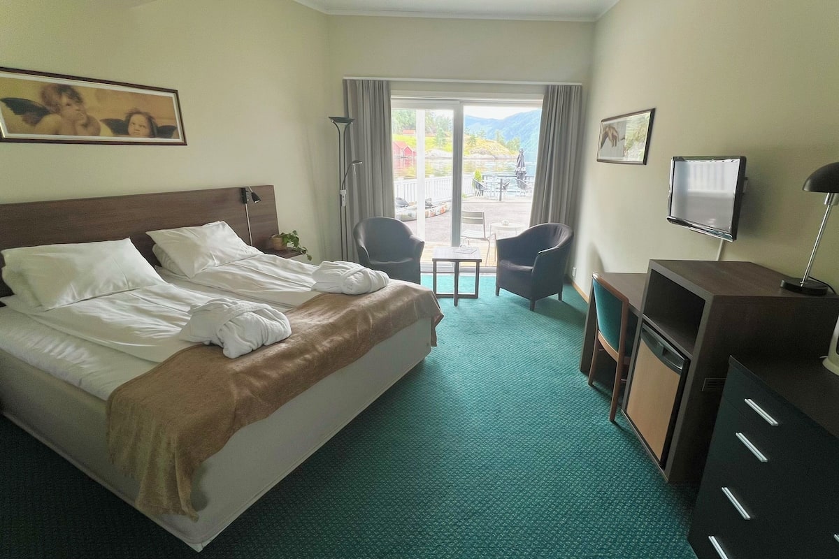 Une chambre d’hôtel avec un lit, un bureau, une chaise, une télévision et une vue sur un lac par la fenêtre.