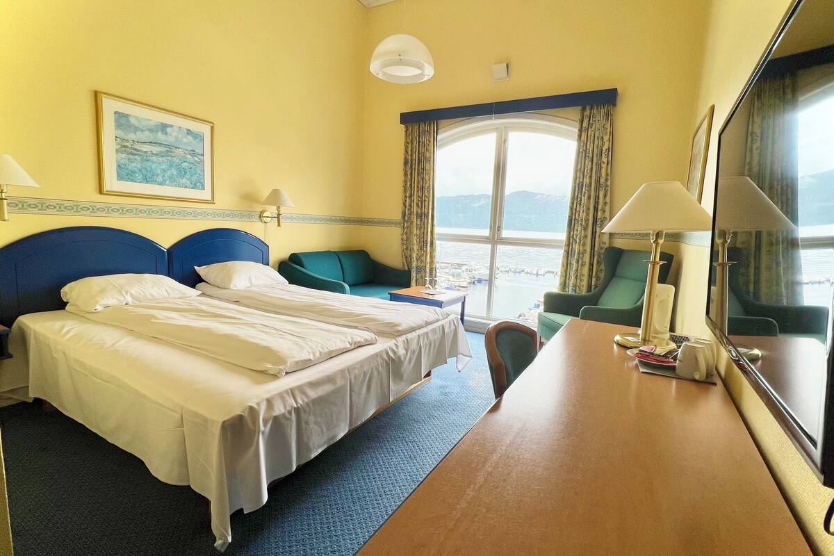 Une chambre d’hôtel comprenant un lit, deux tables de chevet, un bureau, une chaise, une télévision et une fenêtre avec des rideaux.