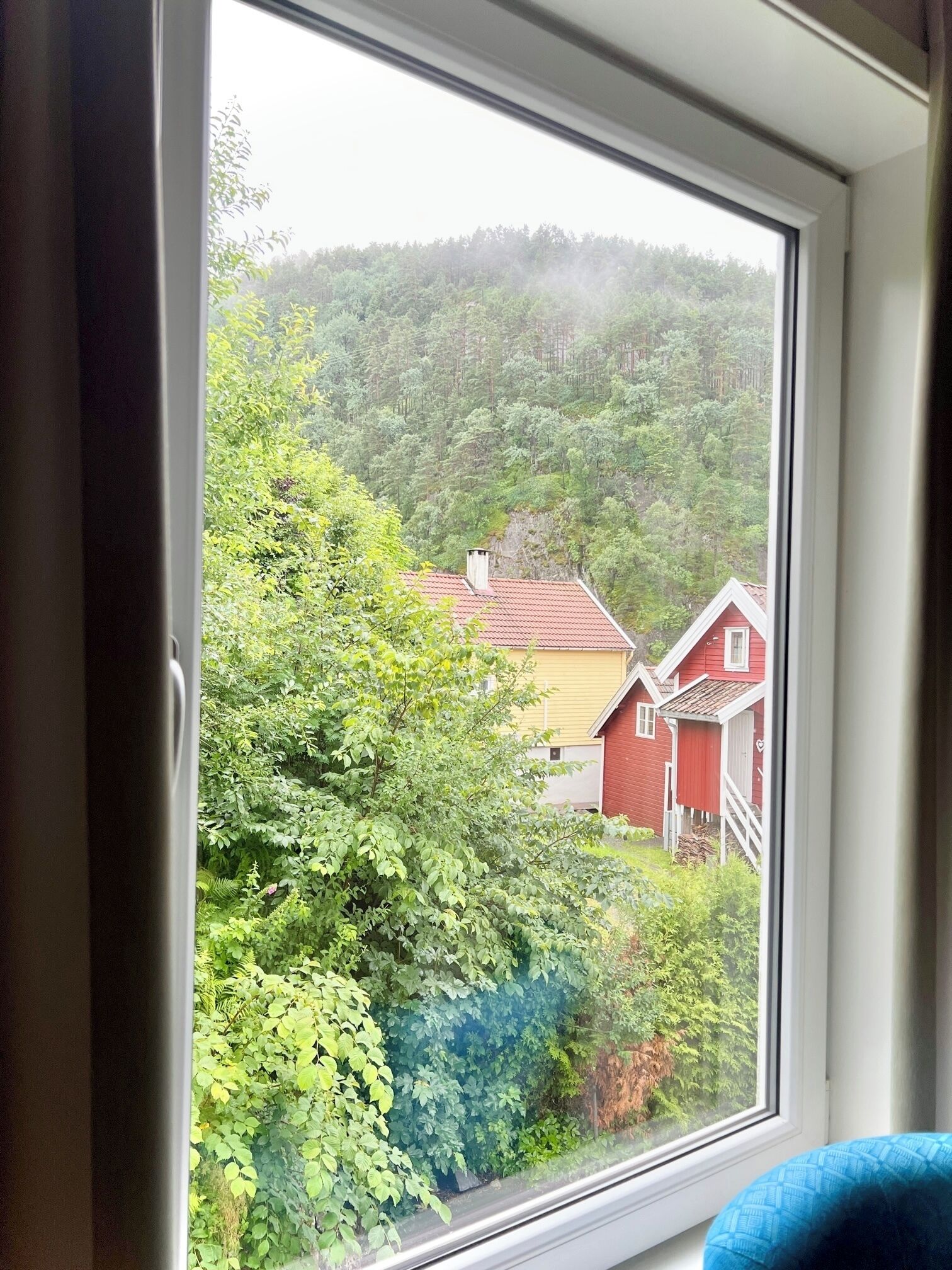 Una ventana con vista a una ladera boscosa y casas rojas.