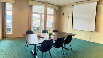 A conference room with a large table, four chairs, a projector screen, and a view of the city through large windows.