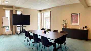 A conference room with a large table, chairs, a whiteboard, a TV, and a potted plant.