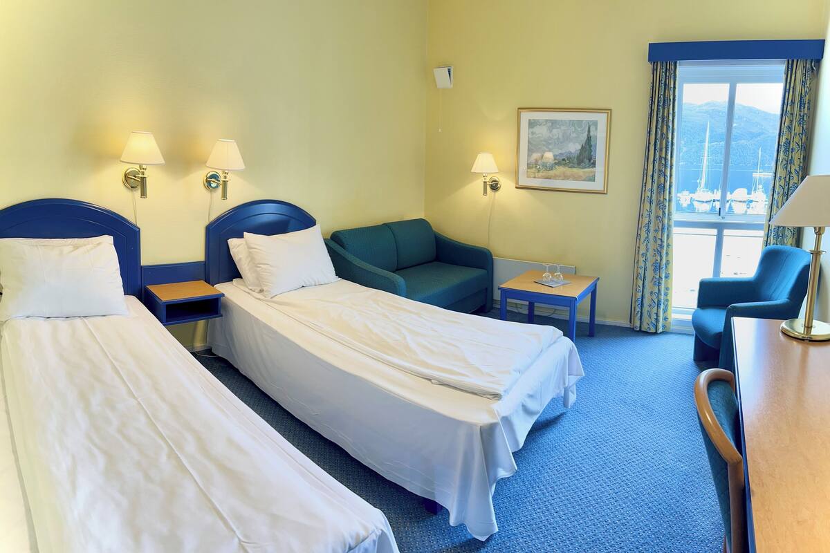 Une chambre d’hôtel avec deux lits simples, un canapé vert, une petite table et une chaise.