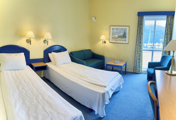 A hotel room with two single beds, a green sofa, a small table, and a chair.